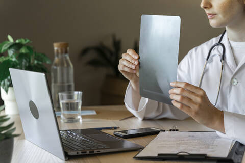 Young female doctor showing x-ray during online consultation on laptop at home office stock photo