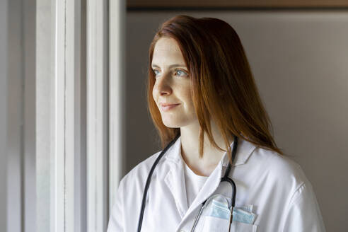 Smiling young female doctor looking through window - AFVF07387