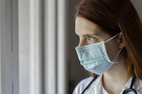 Thoughtful young female doctor wearing face mask during COVID-19 - AFVF07393