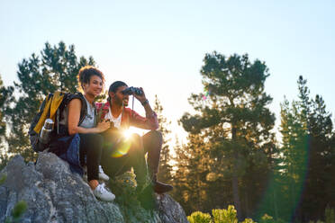 Junges Paar wandert mit dem Fernglas auf Felsen in sonnigen Wäldern - CAIF29825