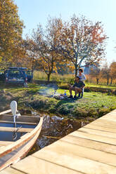 Young couple camping at sunny autumn lakeside - CAIF29826