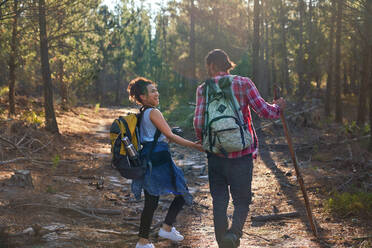Glückliches junges Paar mit Rucksäcken wandert in sonnigen Wäldern - CAIF29830