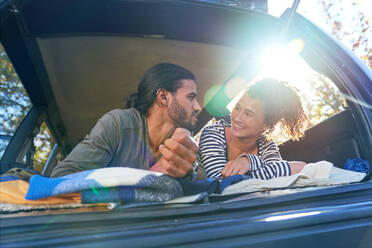 Glückliches junges Paar entspannt sich auf dem Rücksitz eines sonnigen Autos - CAIF29831