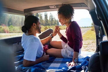 Happy affectionate young couple holding hands in back of sunny car - CAIF29833