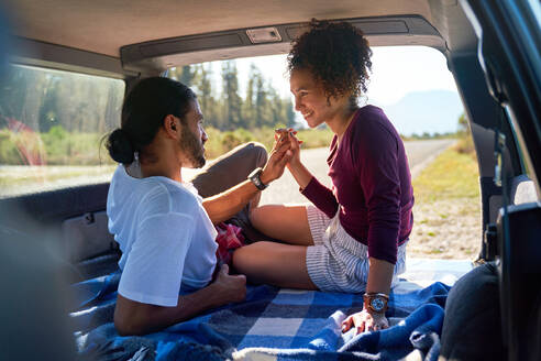 Glückliches, liebevolles, junges Paar hält Hände auf dem Rücksitz eines sonnigen Autos - CAIF29833