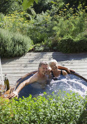 Porträt eines glücklichen älteren Paares, das sich im Whirlpool auf der sonnigen Terrasse entspannt - CAIF29850