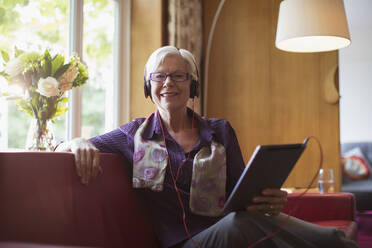 Portrait happy senior woman with headphones and digital tablet on sofa - CAIF29864