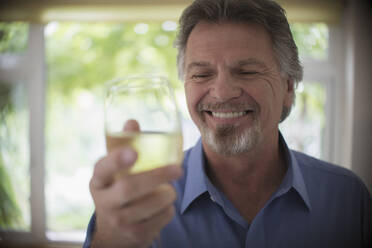 Nahaufnahme eines lächelnden älteren Mannes, der Weißwein trinkt - CAIF29868