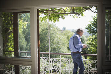 Senior man using digital tablet on sunny idyllic balcony - CAIF29874