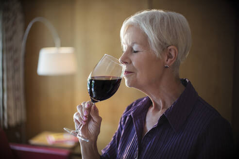 Gelassene ältere Frau, die Rotwein riecht und schmeckt - CAIF29884