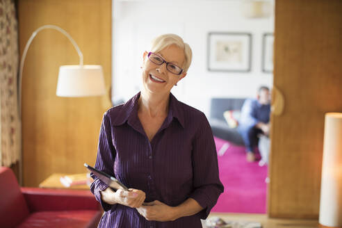 Porträt einer glücklichen selbstbewussten älteren Frau mit digitalem Tablet im Wohnzimmer - CAIF29891