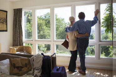 Liebevolles älteres Paar umarmt sich am sonnigen Mietfenster eines Hauses - CAIF29895