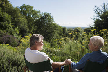 Liebenswertes älteres Ehepaar hält im sonnigen Sommergarten Händchen - CAIF29896