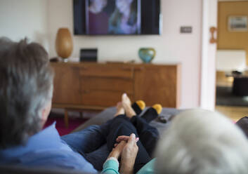 Älteres Ehepaar hält Händchen und schaut auf dem Wohnzimmersofa fern - CAIF29897