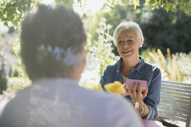 Happy senior woman opening gift from husband on sunny summer patio - CAIF29906