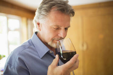 Close up serene man smelling and tasting red wine - CAIF29907