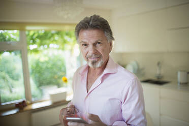 Porträt eines selbstbewussten älteren Mannes mit Smartphone und Tee in der Küche - CAIF29911