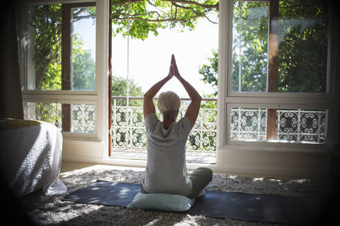 Serene senior woman practicing yoga at sunny tranquil balcony doorway - CAIF29913