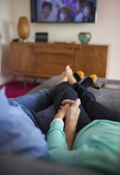 Affectionate couple holding hands and watching TV on sofa - CAIF29920