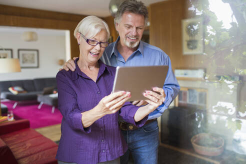 Glückliches älteres Ehepaar benutzt digitales Tablett im Wohnzimmer - CAIF29923
