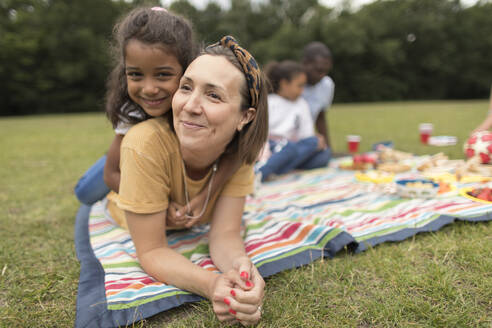 Porträt einer glücklichen Mutter und Tochter, die sich auf einer Picknickdecke im Park entspannen - CAIF29928