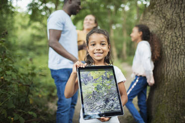 Portraitmädchen hält digitales Tablett mit Foto einer Pflanze im Wald - CAIF29934