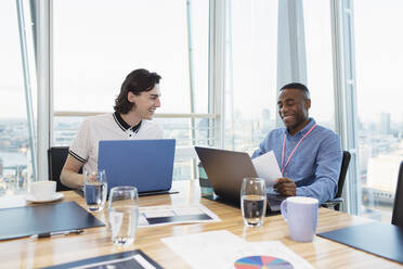 Smiling businessmen working at laptops in highrise conference room - CAIF29969