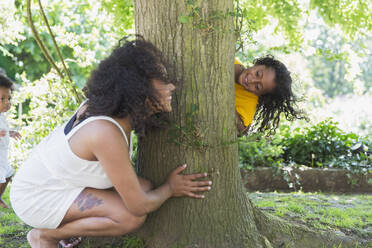 Verspielte Mutter und Tochter spielen Verstecken am Baum - CAIF29984