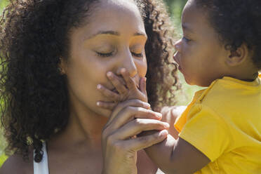Nahaufnahme einer liebevollen Mutter, die die Hand einer Kleinkind-Tochter küsst - CAIF29986