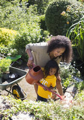 Mutter und Tochter gießen Pflanzen im sonnigen Sommergarten - CAIF29998