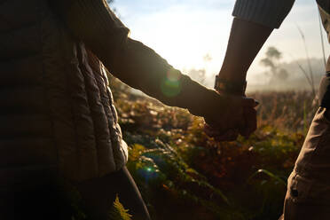 Close up silhouette young couple holding hands on sunny hike in nature - CAIF30007