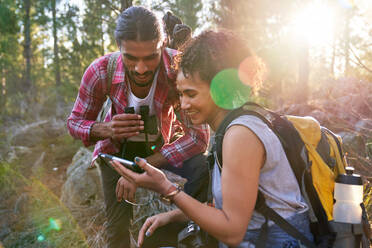 Glückliches junges Wanderpaar mit Smartphone in sonnigen Wäldern - CAIF30010
