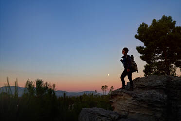 Junge Wanderin auf Fels in landschaftlich ruhiger Wüste in der Abenddämmerung - CAIF30018