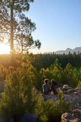 Junges Wandererpaar geniesst bei Sonnenuntergang sonnige Aussicht auf Bäume im Wald - CAIF30019