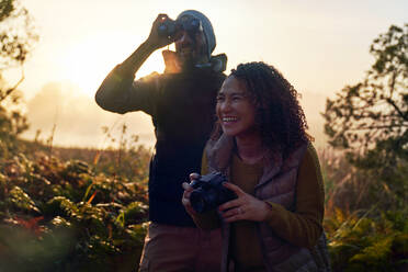 Glückliches junges Wanderpaar mit Kamera und Fernglas in der Natur - CAIF30020
