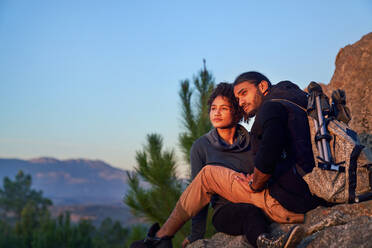 Serene young hiking couple enjoying sunset on rocks - CAIF30036