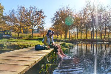 Glückliches junges Paar auf dem Dock taucht barfuss in sonnigen Herbstsee - CAIF30044