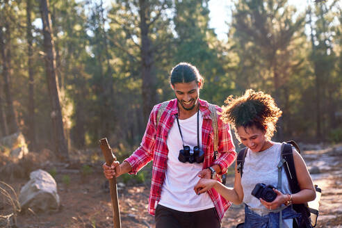 Glückliches junges Paar wandert mit Fernglas und Kamera in sonnigen Wäldern - CAIF30047