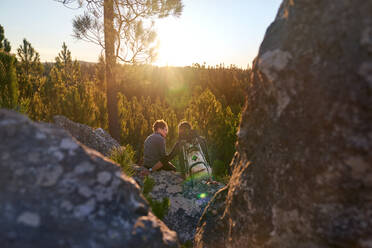 Affectionate young hiker couple relaxing on rock in sunny sunset woods - CAIF30070