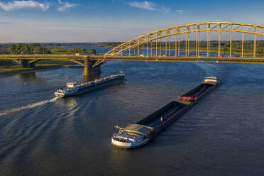 Niederlande, Gelderland, Nijmegen, Luftaufnahme eines Lastkahns und eines Containerschiffs, die unter einer Brücke auf dem Fluss Waal fahren - HAMF00776