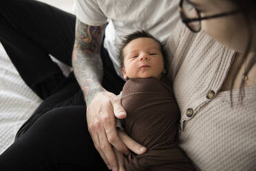 Neugeborener Junge in braun gewickelt, gehalten von tätowierten Hipster-Eltern - CAVF90139