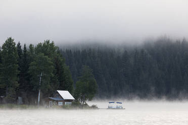Wooden cabin on lake shore on foggy morning in British Columbia - CAVF90167