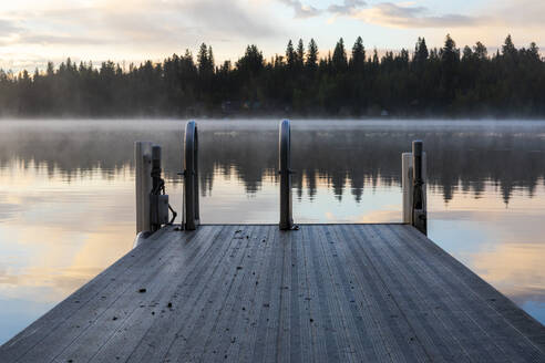 Schwimmsteg mit Leiter in der Nähe eines ruhigen Sees bei Sonnenuntergang mit Reflexion - CAVF90170