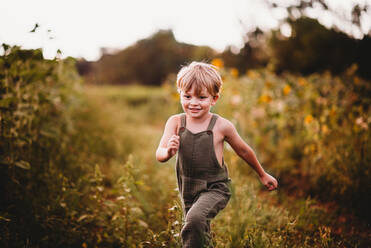 Smiling boy running in a field with sunflowers in the background - CAVF90173
