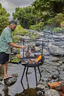 Chefkoch bereitet Steak über offenem Feuer vor Grill in der Nähe des Bachbettes - CAVF90183