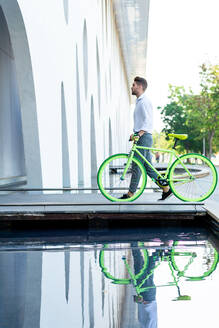 Side view of a young bearded man walking with fixie bike - CAVF90202
