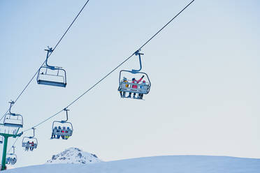 Skiers on a chairlift looking down with a blue background - CAVF90214