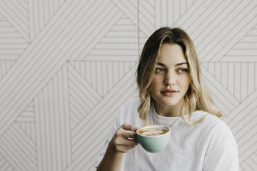 Young woman looking away while drinking coffee in cafe - LHPF01298