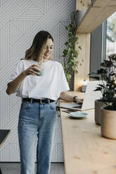 Junge Frau trinkt Kaffee und arbeitet am Laptop in einem Café - LHPF01308