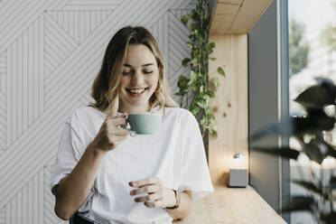 Lächelnde junge Frau, die eine Kaffeetasse hält, während sie in einem Cafe steht - LHPF01310